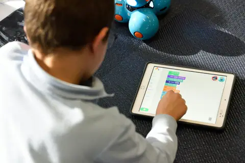 A child using a learning app on a tablet, with a coding robot beside them.