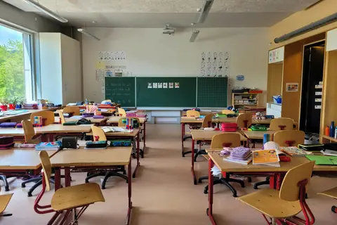 An empty primary school classroom with small chairs stacked beside low desks.