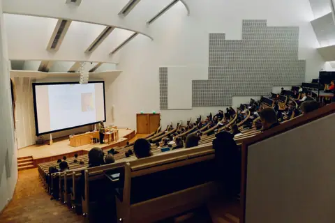A raked university lecture theatre with rows of desks facing a projection screen.
